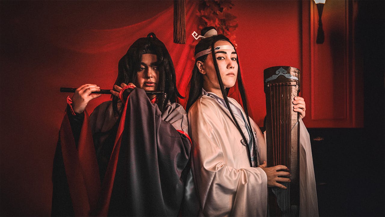 Two individuals in traditional Asian cosplay costumes, poised against a dramatic red backdrop.